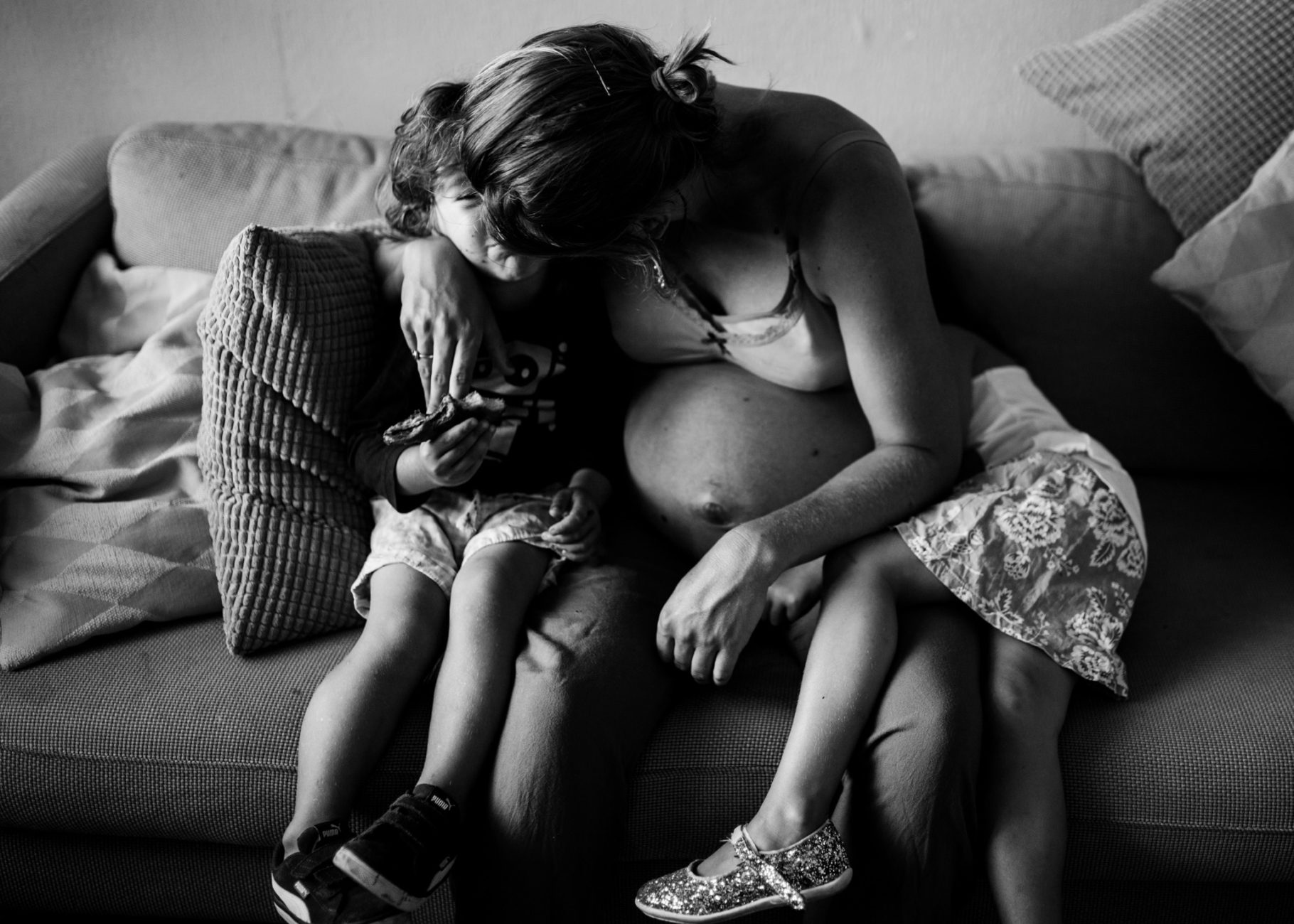 Pregnant mom sitting on the couch in her living room. She's with her two kids, kissing her boy while hugging him. Her daughter is hugging her. Picture in black and white. Amsterdam family and newborn photographer.