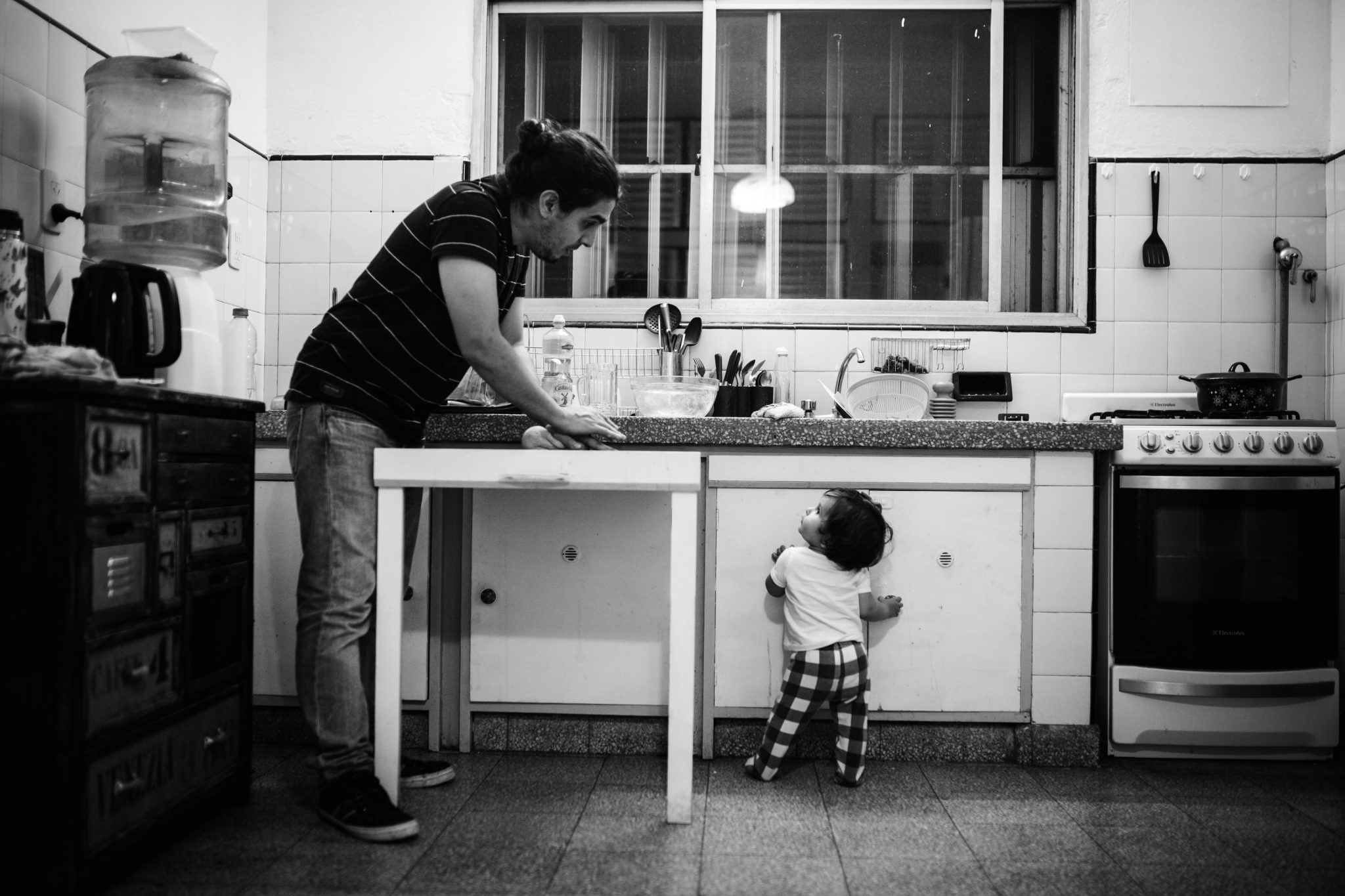 Dad cooking in the kitchen with his little toddler. Both standing, looking at each other, having a conversation. Picture in black and white. Day in the life, documentary family and baby photographer amsterdam, netherlands