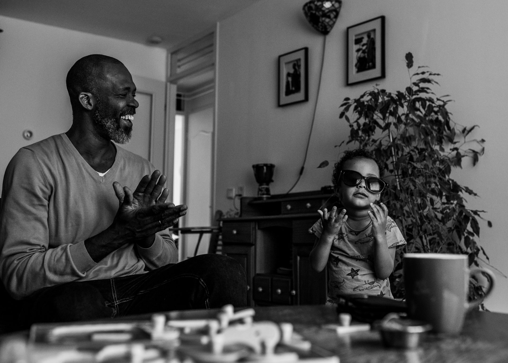 Black and White picture, toddler playing with his father sunglasses while dad's giving an applause and laughing. Documentary photoshoot in Amsterdam